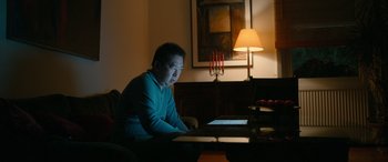 Movie still from “Luther: The Fallen Sun” (2023), directed by Jamie Payne – A man sitting in front of a computer at a table; Medium shot, Low angle