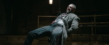 Movie still from “Luther: The Fallen Sun” (2023), directed by Jamie Payne – An old man is sitting on a swing in the dark; Wide shot, Low angle