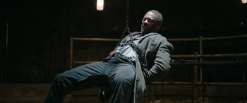 Movie still from “Luther: The Fallen Sun” (2023), directed by Jamie Payne – A man in a suit and tie on a swing; Medium shot, High angle
