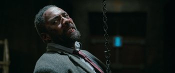 Movie still from “Luther: The Fallen Sun” (2023), directed by Jamie Payne – A man in a suit and tie is sitting on a swing; Close Up shot, Low angle