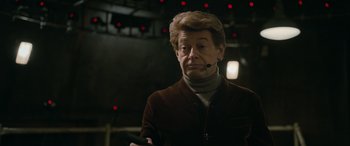 Movie still from “Luther: The Fallen Sun” (2023), directed by Jamie Payne – An older man wearing a brown jacket and a headset; Close Up shot, Over the shoulder angle