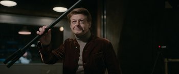 Movie still from “Luther: The Fallen Sun” (2023), directed by Jamie Payne – An older man wearing a brown jacket and a brown sweater; Medium shot, Over the shoulder angle