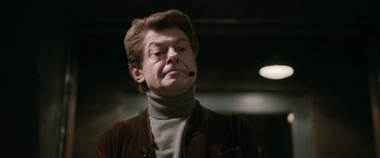 Movie still from “Luther: The Fallen Sun” (2023), directed by Jamie Payne – A man wearing a brown jacket with a microphone in his mouth; Close Up shot, Low angle