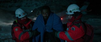 Movie still from “Luther: The Fallen Sun” (2023), directed by Jamie Payne – A man wrapped in a blue blanket in front of two other men; Medium shot, High angle
