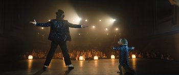 Movie still from “Lyle, Lyle, Crocodile” (2022), directed by Will Speck – A man and a child performing on a stage; Extreme Wide shot, Low angle