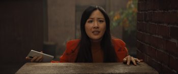 Movie still from “Lyle, Lyle, Crocodile” (2022), directed by Will Speck – A woman sitting at a wooden table in front of a brick wall; Medium shot, Low angle