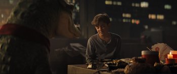 Movie still from “Lyle, Lyle, Crocodile” (2022), directed by Will Speck – A man sitting at a table with a dinosaur in the background; Medium shot, Over the shoulder angle