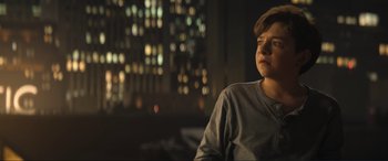 Movie still from “Lyle, Lyle, Crocodile” (2022), directed by Will Speck – A young man sitting in a room with a city skyline in the background; Medium shot, Low angle