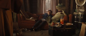 Movie still from “Lyle, Lyle, Crocodile” (2022), directed by Will Speck – A person sitting on a couch next to a stuffed animal; Wide shot, High angle