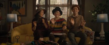 Movie still from “Lyle, Lyle, Crocodile” (2022), directed by Will Speck – Three people sitting on a yellow couch and wearing hats; Medium shot, Over the shoulder angle