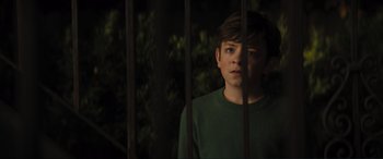 Movie still from “Lyle, Lyle, Crocodile” (2022), directed by Will Speck – A young boy standing behind bars in front of trees; Close Up shot, High angle