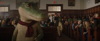 Movie still from “Lyle, Lyle, Crocodile” (2022), directed by Will Speck – A man in a courtroom with a fake alligator in front of a crowd of onlookers; Wide shot, Over the shoulder angle