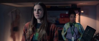 Movie still from “M3GAN” (2022), directed by Gerard Johnstone – A woman with long brown hair wearing a plaid shirt; Medium shot, Over the shoulder angle