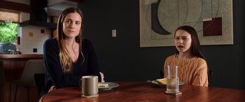 Movie still from “M3GAN” (2022), directed by Gerard Johnstone – A woman sitting at a table with a plate of food and a mug; Medium shot, Over the shoulder angle