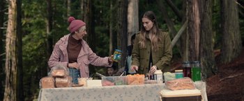 Movie still from “M3GAN” (2022), directed by Gerard Johnstone – A woman handing food to another woman at an outdoor gathering; Medium shot, Over the shoulder angle