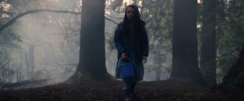 Movie still from “M3GAN” (2022), directed by Gerard Johnstone – A woman holding a blue bucket in the woods; Medium shot, Low angle