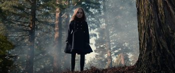 Movie still from “M3GAN” (2022), directed by Gerard Johnstone – A girl in a black coat standing in the woods; Medium shot, Low angle
