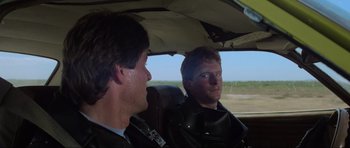 Movie still from “Mad Max” (1979), directed by George Miller – Two men sitting in the back seat of a car; Close Up shot, Over the shoulder angle
