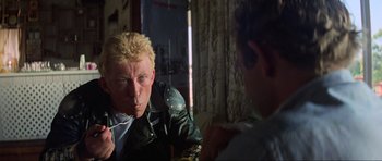 Movie still from “Mad Max” (1979), directed by George Miller – A man in a leather jacket is smoking a cigarette in front of a mirror; Close Up shot, Over the shoulder angle