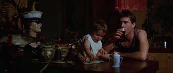 Movie still from “Mad Max” (1979), directed by George Miller – A man and a baby sitting at a table; Medium shot, High angle