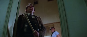 Movie still from “Mad Max” (1979), directed by George Miller – A man holding a baseball bat while standing next to another man; Medium shot, Low angle