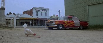 Movie still from “Mad Max” (1979), directed by George Miller – An old car is parked on the side of the road; Wide shot, Low angle