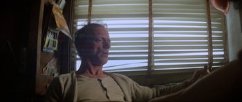 Movie still from “Mad Max” (1979), directed by George Miller – An older man sitting in front of a window; Close Up shot, Low angle