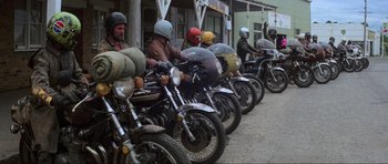 Movie still from “Mad Max” (1979), directed by George Miller – A row of motorcycles parked on the side of the street; Wide shot, High angle