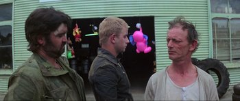 Movie still from “Mad Max” (1979), directed by George Miller – A group of men standing next to each other; Medium shot, Over the shoulder angle