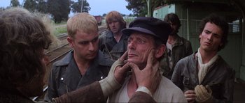 Movie still from “Mad Max” (1979), directed by George Miller – A man with a hat is touching his face; Close Up shot, Over the shoulder angle
