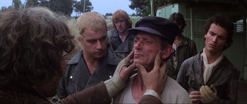 Movie still from “Mad Max” (1979), directed by George Miller – A man with a hat is touching another man's ear; Close Up shot, Over the shoulder angle