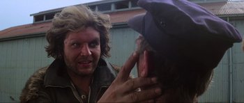 Movie still from “Mad Max” (1979), directed by George Miller – A man with long hair and a hat is talking to another man with long brown hair; Close Up shot, Over the shoulder angle