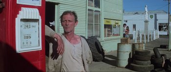 Movie still from “Mad Max” (1979), directed by George Miller – A man standing in front of a green building; Medium shot, Low angle