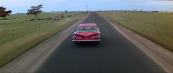 Movie still from “Mad Max” (1979), directed by George Miller – A red car is driving down the street; Wide shot, High angle