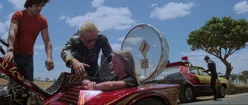 Movie still from “Mad Max” (1979), directed by George Miller – A man helping a girl in a fire truck; Medium shot, Over the shoulder angle