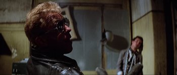Movie still from “Mad Max” (1979), directed by George Miller – A man wearing glasses and a leather jacket looking up; Close Up shot, Over the shoulder angle