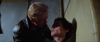 Movie still from “Mad Max” (1979), directed by George Miller – A man with glasses is touching another man's face; Close Up shot, Over the shoulder angle
