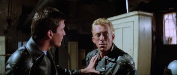 Movie still from “Mad Max” (1979), directed by George Miller – A man in a black leather jacket talking to another man in a black leather jacket; Medium shot, Over the shoulder angle