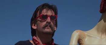 Movie still from “Mad Max” (1979), directed by George Miller – A person wearing sunglasses and a mustache; Close Up shot, Low angle