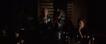Movie still from “Mad Max” (1979), directed by George Miller – A man and a woman sitting in a dark room; Medium shot, Low angle