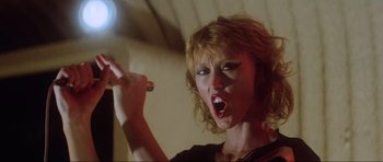 Movie still from “Mad Max” (1979), directed by George Miller – A woman is singing into a microphone; Close Up shot, Low angle