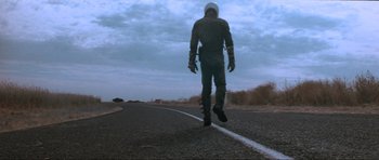 Movie still from “Mad Max” (1979), directed by George Miller – A man in a helmet is walking down the street; Wide shot, Low angle