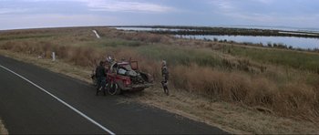 Movie still from “Mad Max” (1979), directed by George Miller – Two people on the side of the road near a car that has been broken down; Extreme Wide shot, High angle