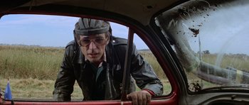 Movie still from “Mad Max” (1979), directed by George Miller – A man wearing a helmet looking out of the window of a car; Close Up shot, Low angle