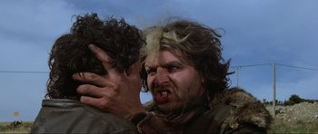 Movie still from “Mad Max” (1979), directed by George Miller – A man with long hair is holding another man's face; Close Up shot, Low angle