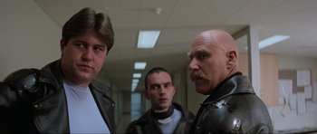 Movie still from “Mad Max” (1979), directed by George Miller – A group of men standing next to each other in a hallway; Close Up shot, Low angle