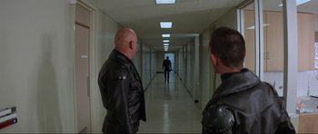 Movie still from “Mad Max” (1979), directed by George Miller – Two men in leather jackets in an empty hallway; Wide shot, Over the shoulder angle