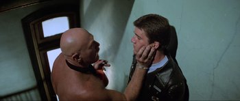 Movie still from “Mad Max” (1979), directed by George Miller – A man putting a tattoo on another man's ear; Close Up shot, Over the shoulder angle