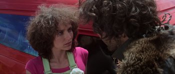 Movie still from “Mad Max” (1979), directed by George Miller – A man and a woman standing next to each other in front of a red car; Close Up shot, Over the shoulder angle