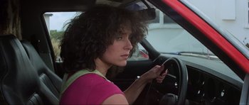 Movie still from “Mad Max” (1979), directed by George Miller – A woman sitting in the drivers seat of a car while holding a cell phone; Close Up shot, Low angle